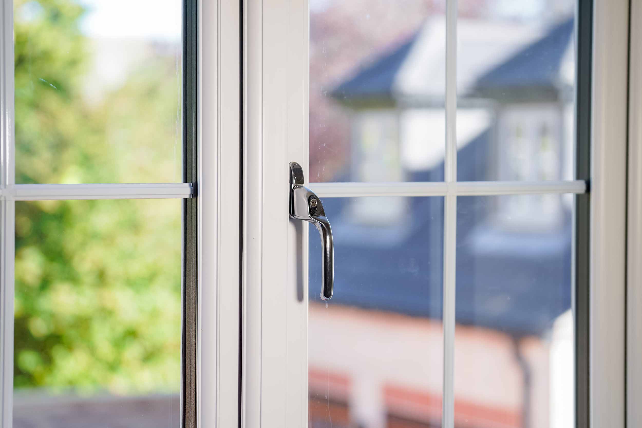 Close up image of a white casement window and handle. 